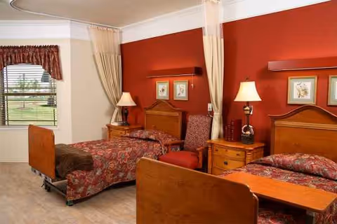 Two wooden twin beds with red floral bedspreads, nightstands, lamps, and a red wall.