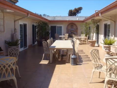 Outdoor courtyard with tables, chairs, plants, and a fountain along the walls.