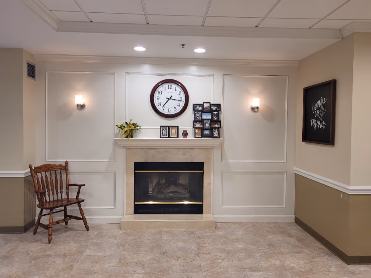 Interior common area with a fireplace, wall clock, framed photos, a wooden chair, and wall sconces.