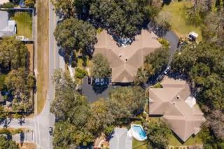 Aerial view of a residential facility with multiple buildings surrounded by trees and parking areas, adjacent to a road.