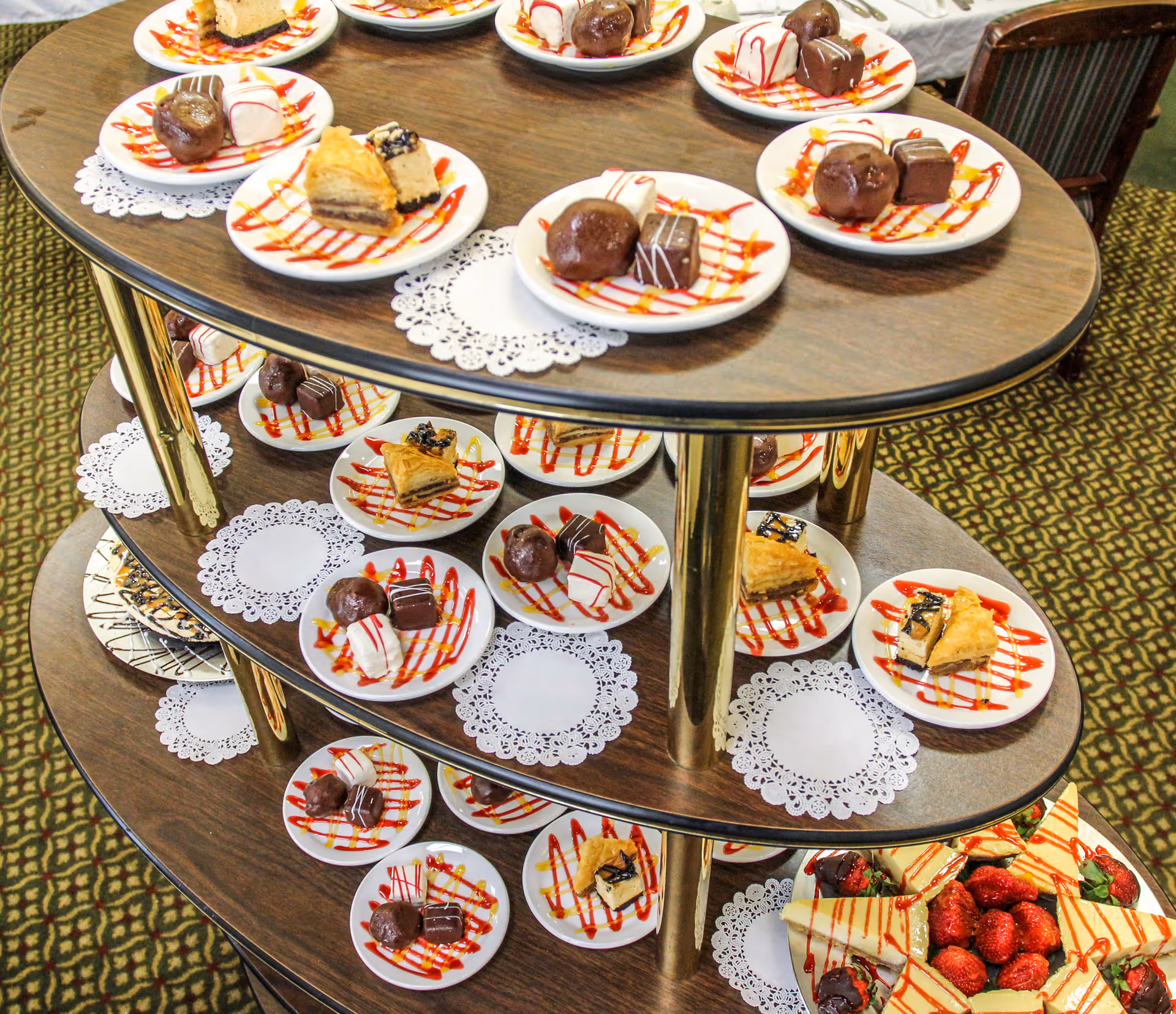 Tiered serving cart filled with small plates of assorted desserts drizzled with sauce and a bowl of strawberries.