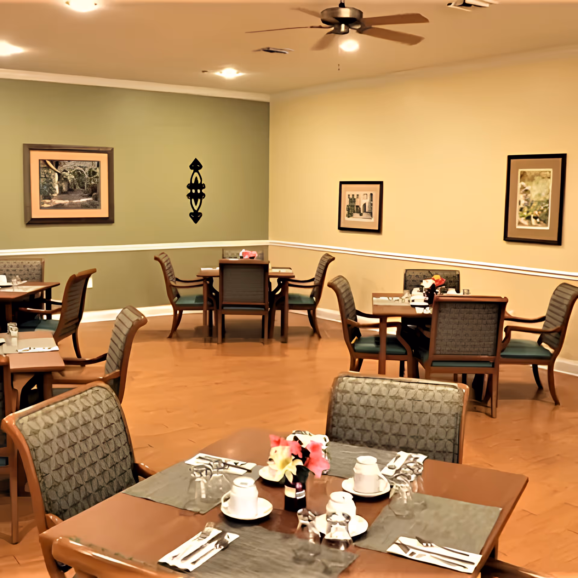 Dining room with multiple set tables and chairs, place settings, and framed artwork on the walls.