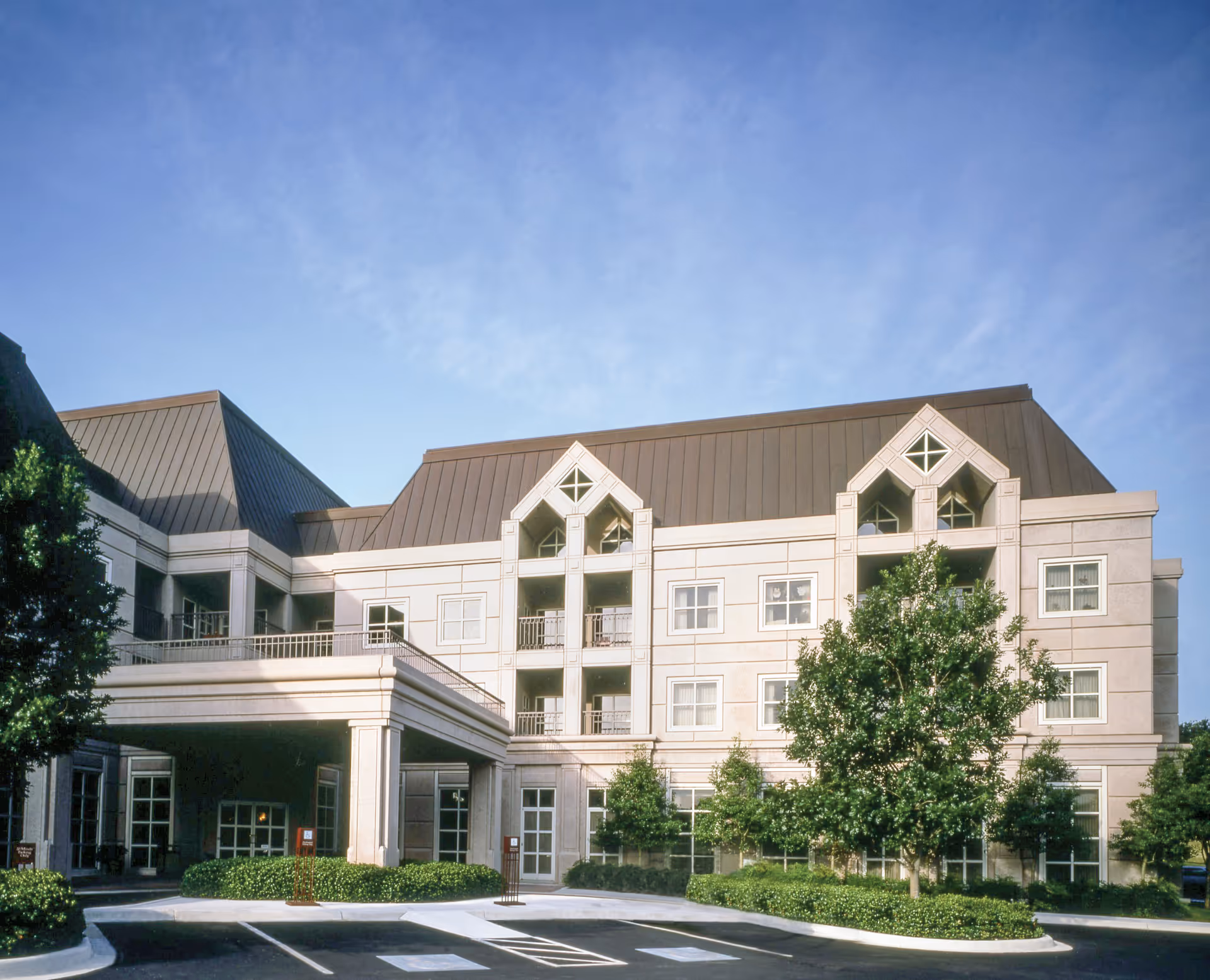 Beige multi-story building with peaked roofs, an inviting entrance canopy, and surrounding landscaping.