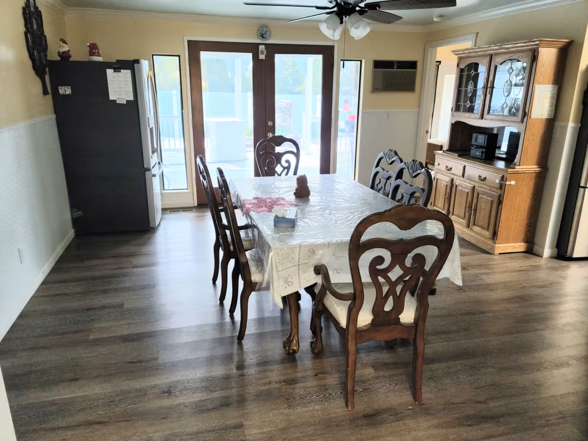 Dining room with a wooden table and six chairs on laminate flooring, a china cabinet and refrigerator, and glass doors leading outside.