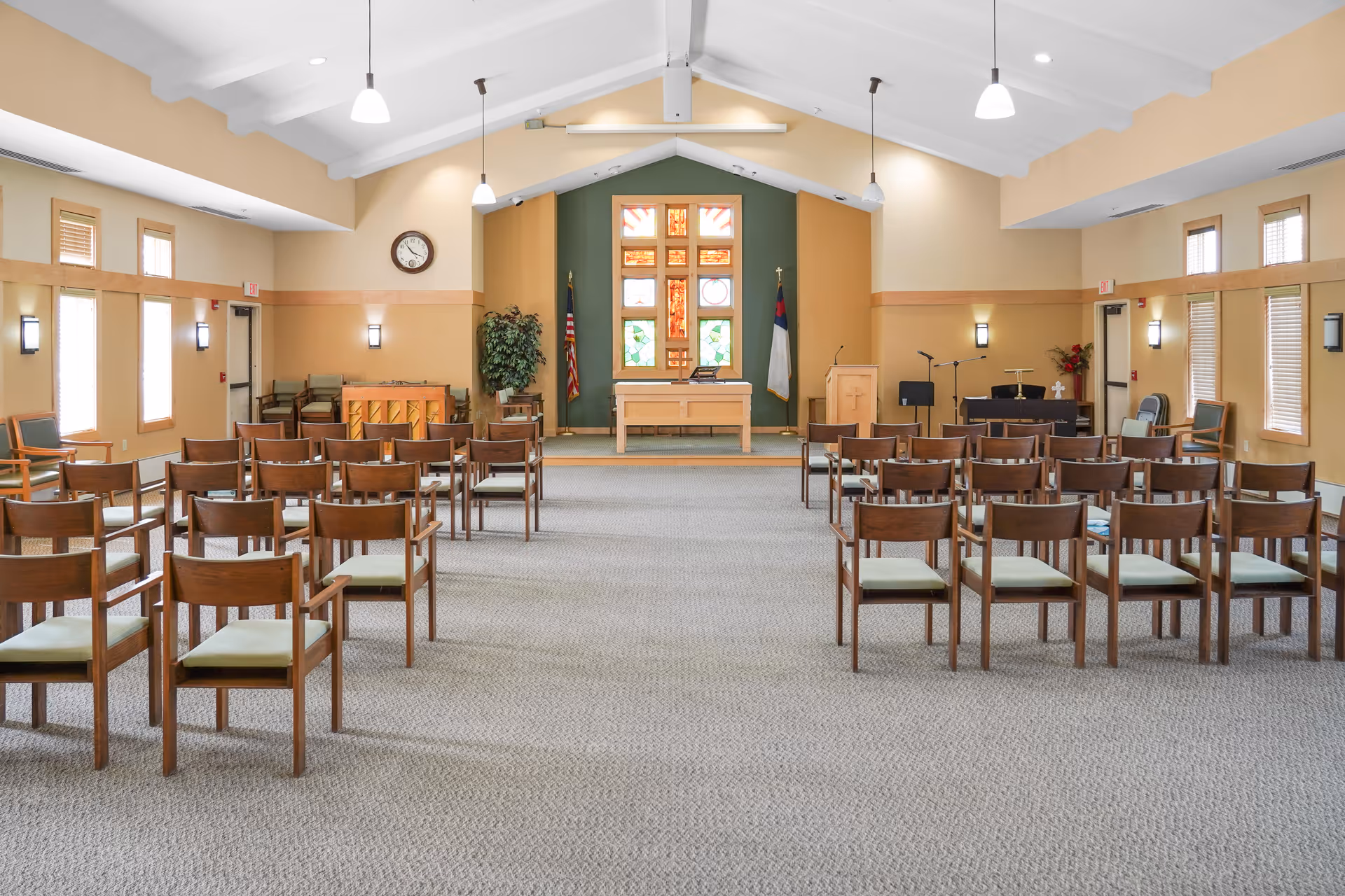 Spacious chapel-style meeting room with rows of wooden chairs facing an altar and stained-glass window.