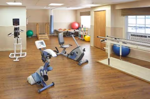Indoor therapy gym with exercise bikes, parallel bars, stability balls, and equipment for rehabilitation.
