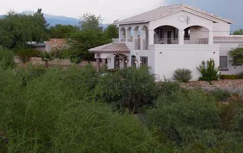 Mediterranean-style white two-story building with arches amid desert shrubs