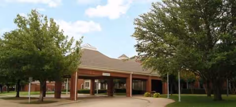 Brick senior living facility with a covered entrance and trees under a blue sky