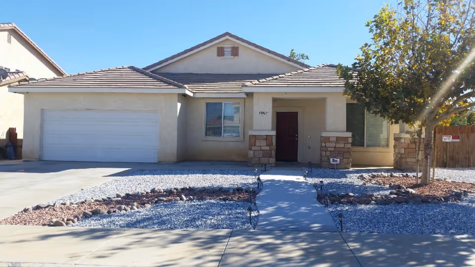 Single-story ranch-style house front with a two-car garage, walkway, and gravel landscaping.