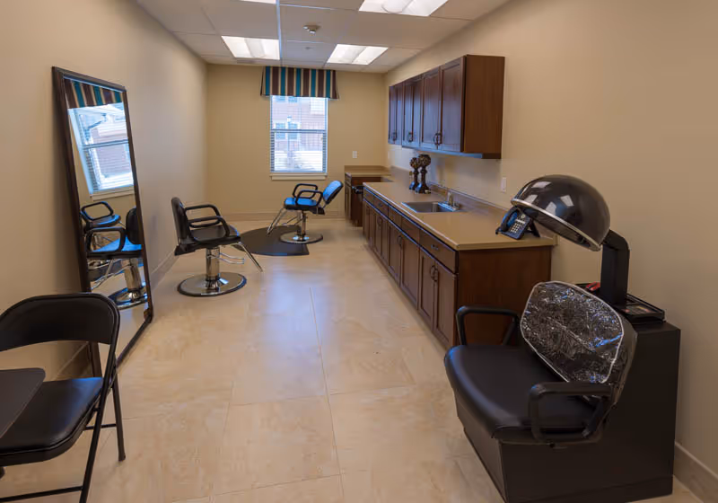 Small on-site salon with styling chairs, a full-length mirror, dryer station, and cabinetry along one wall.
