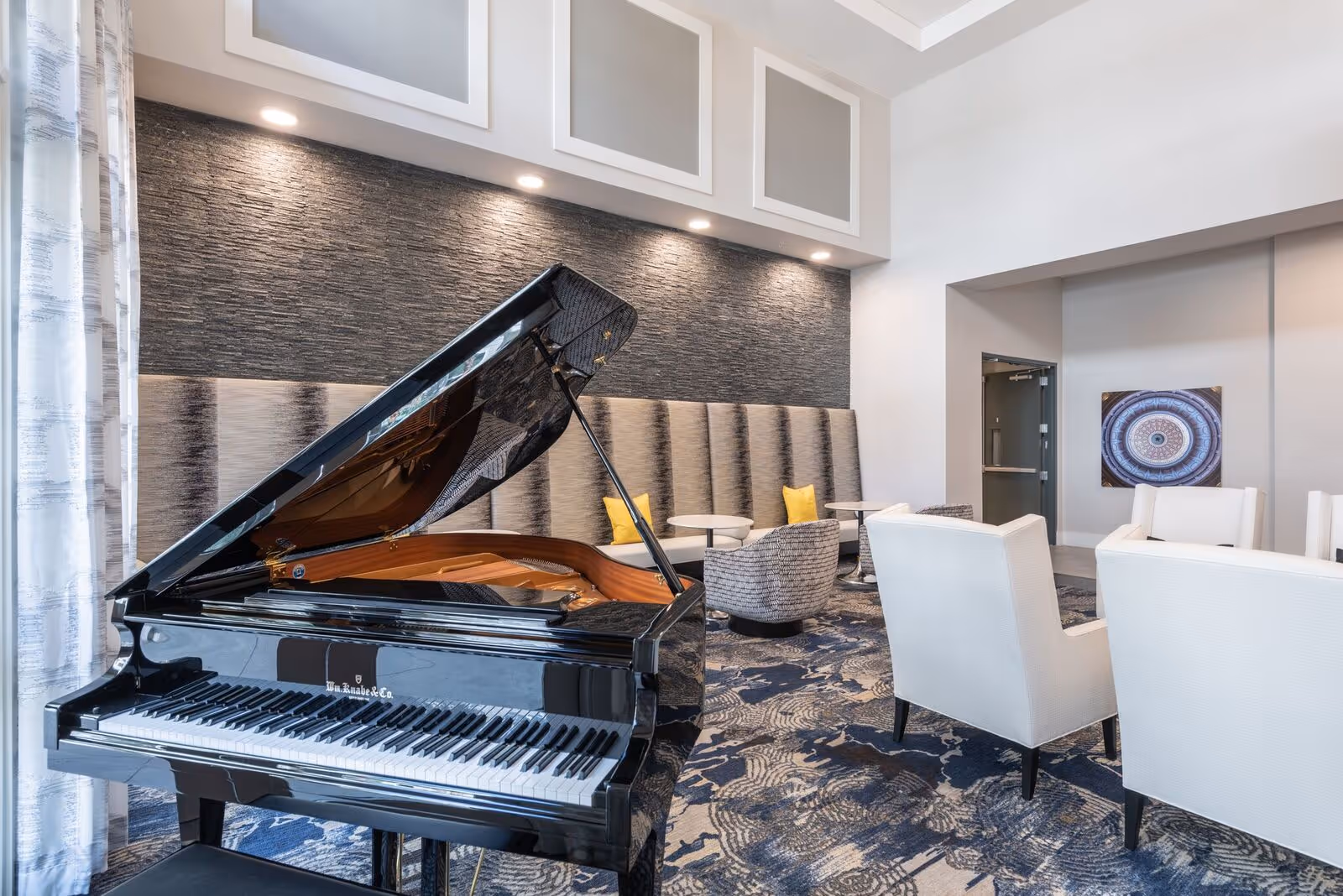 Modern lounge with a black grand piano in the foreground and upholstered seating and tables in the background.