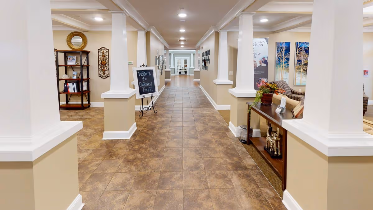 Bright, spacious tiled corridor with white columns, decorative shelving, and seating in a senior living facility lobby.