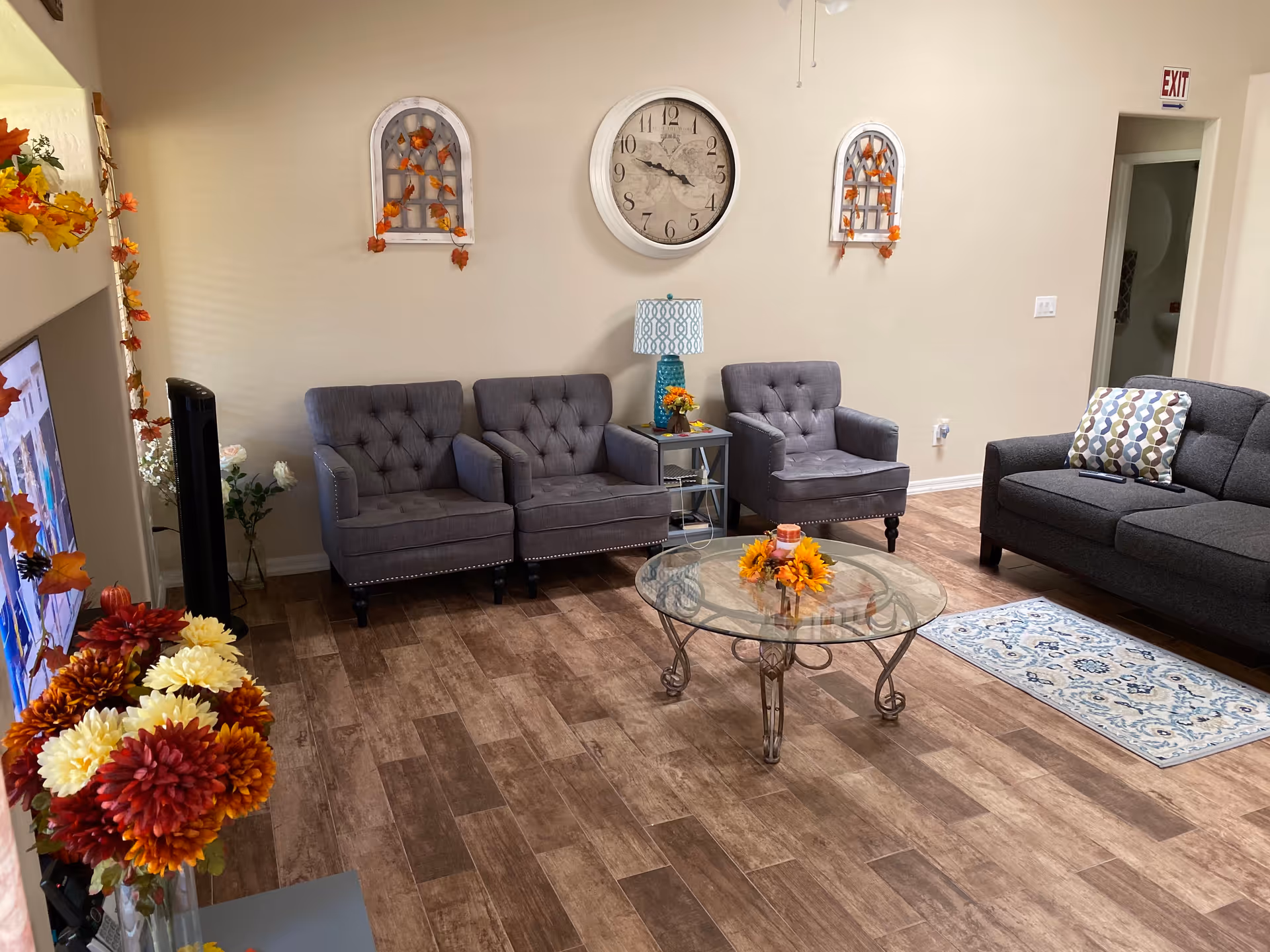 Living room with gray upholstered chairs and sofa arranged around a glass coffee table with fall-themed decorations.
