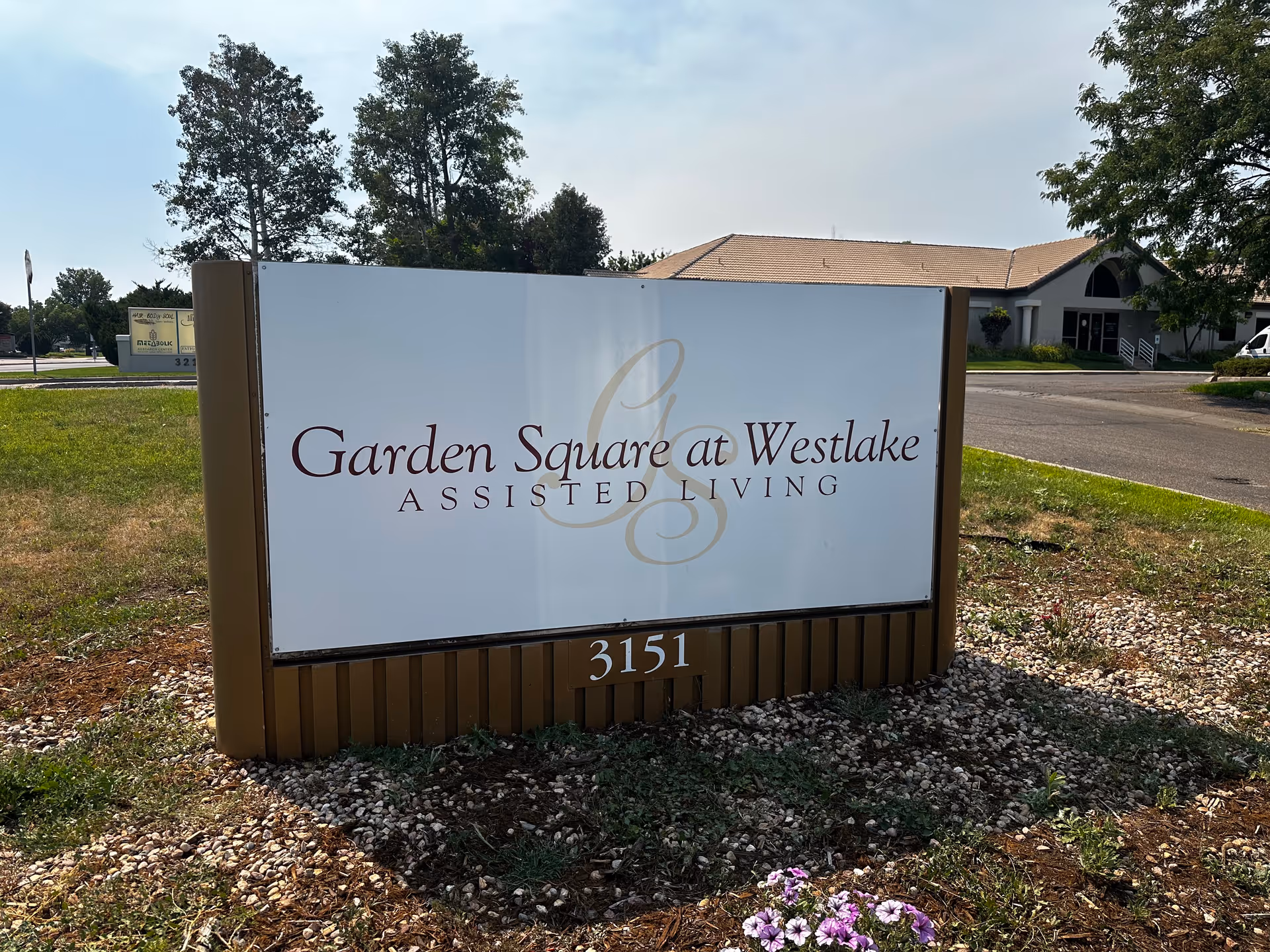 Outdoor sign reading "Garden Square at Westlake Assisted Living" with the facility building visible behind it.