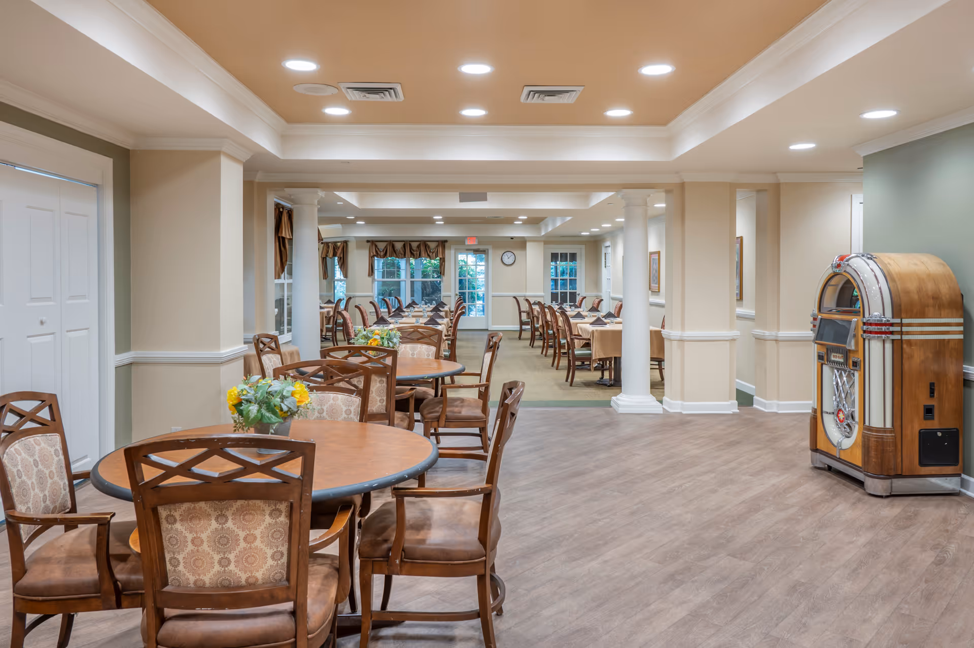 Spacious dining room with round wooden tables and chairs, columns, and a vintage jukebox.