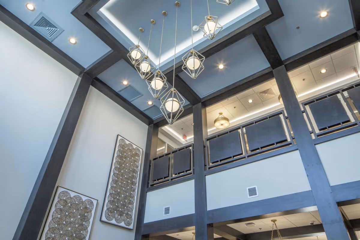 High-ceilinged interior atrium with hanging geometric pendant lights, dark beams, balcony railing and decorative wall art.