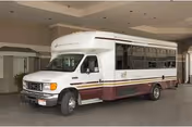 White and maroon passenger shuttle bus parked under a covered facility entrance.