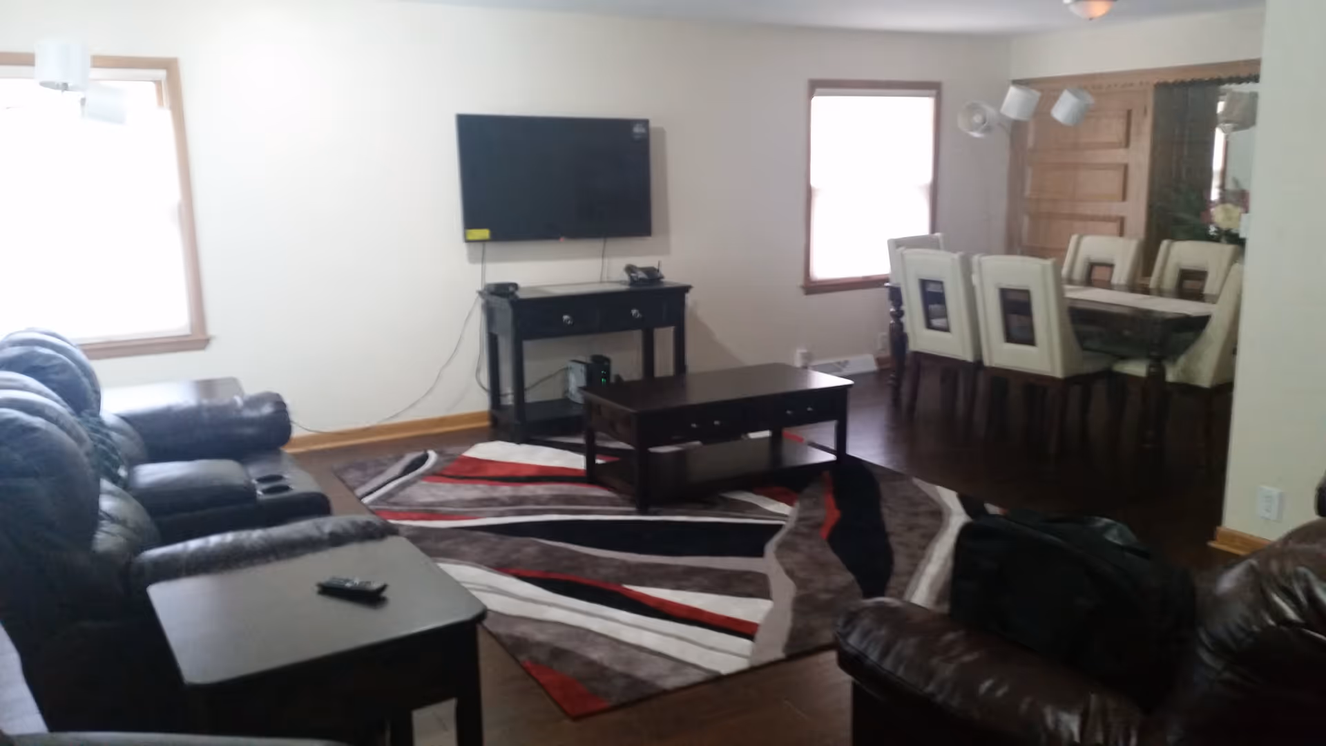 Open-plan living room with leather sofas, a patterned area rug, wall-mounted TV and an adjacent dining table with chairs.