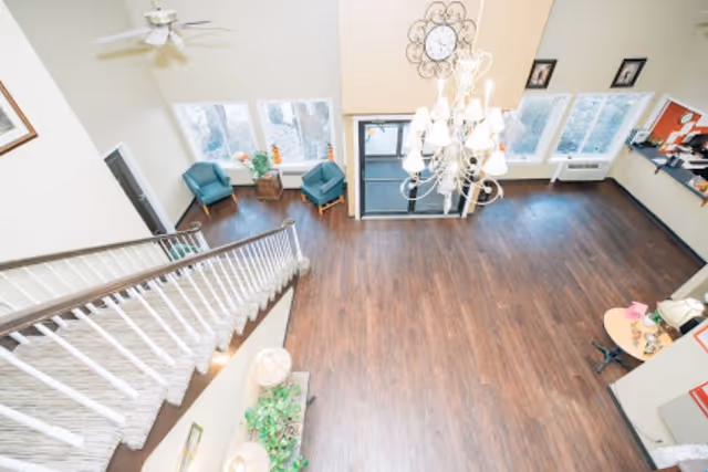 High-angle view of a spacious entry lobby with hardwood floors, a staircase, chandelier, seating area, and front doors.