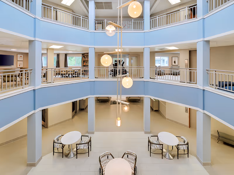 Open multi-level atrium with hanging pendant lights, ground-floor seating tables, and upper-level balconies overlooking the lobby.
