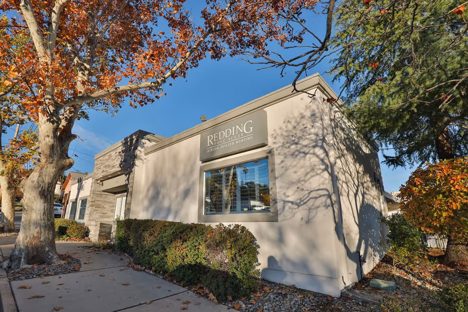 Exterior front of the Redding Post Acute building with a sidewalk, trees, and shrubbery in front.