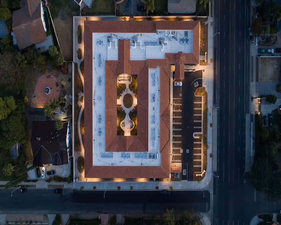 Aerial view of The Preserve at Woodland Hills Assisted Living & Memory Care building at dusk, showing a rectangular structure with a central courtyard, surrounded by a parking lot and adjacent streets.