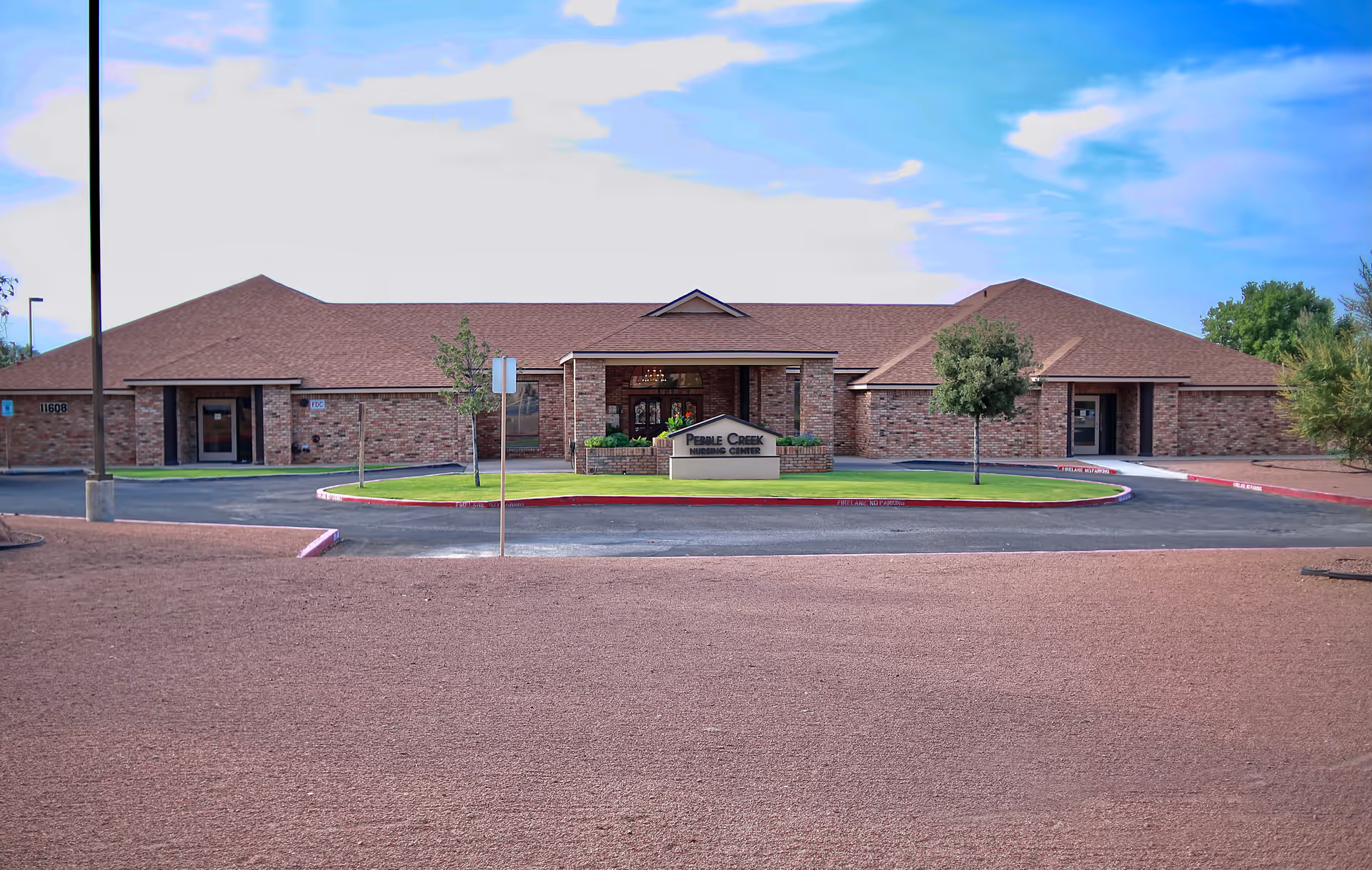 Front exterior of a single-story brick nursing center with a circular driveway and a sign reading 'Pebble Creek Nursing Center'.