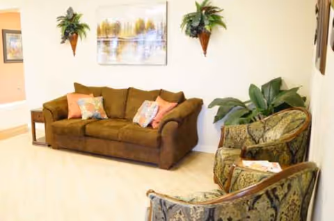 A brown sofa and patterned chairs surround a calm living room with plants and wall art.