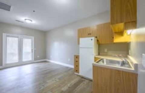 Studio-style interior room featuring a small kitchenette with a refrigerator and sink, wood flooring, and double glass doors.