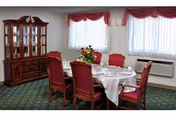 Formal dining room with a round table set for six, red upholstered chairs, a china cabinet, and windows with red valances.
