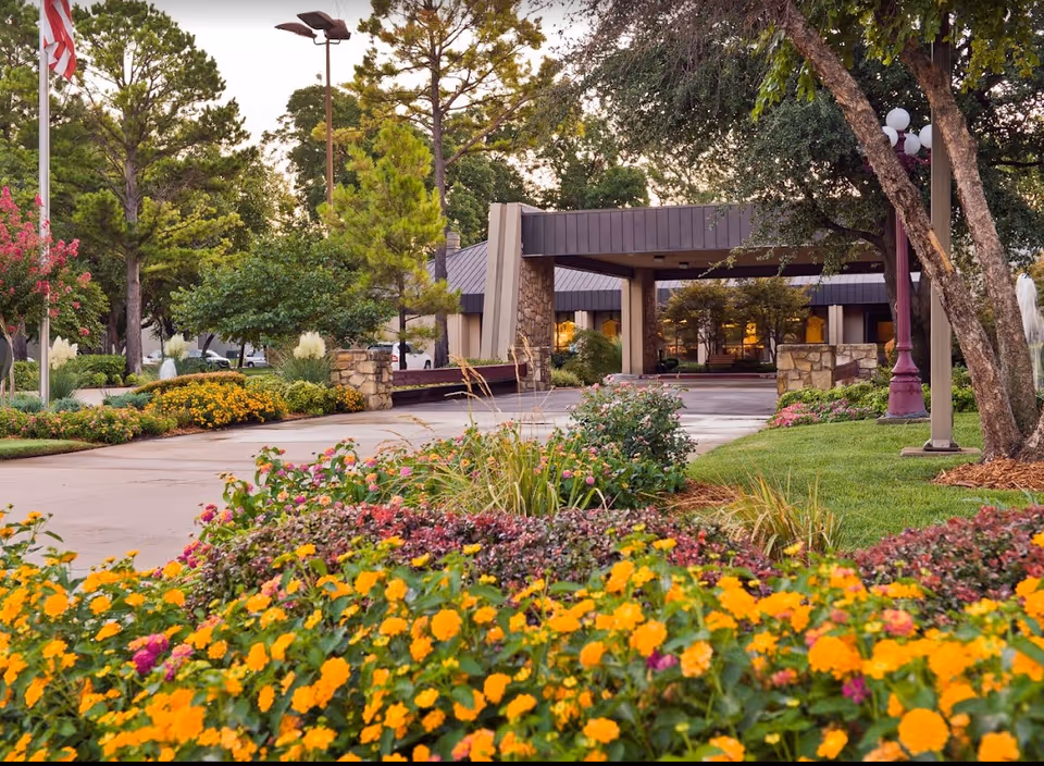 Front entrance and driveway of a senior living facility with landscaped flowerbeds and a covered porte-cochère.