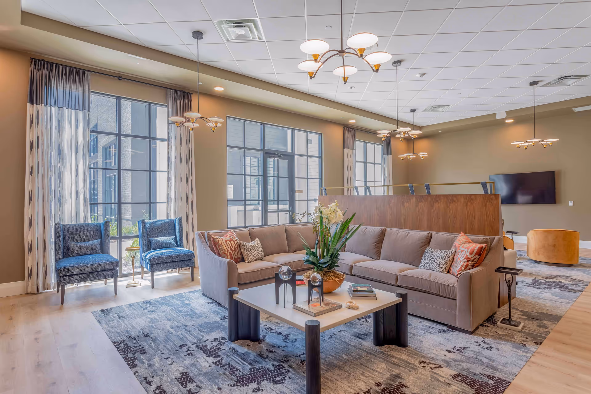 Bright modern lounge with a sectional sofa, coffee table, armchairs, large windows, and pendant lighting.