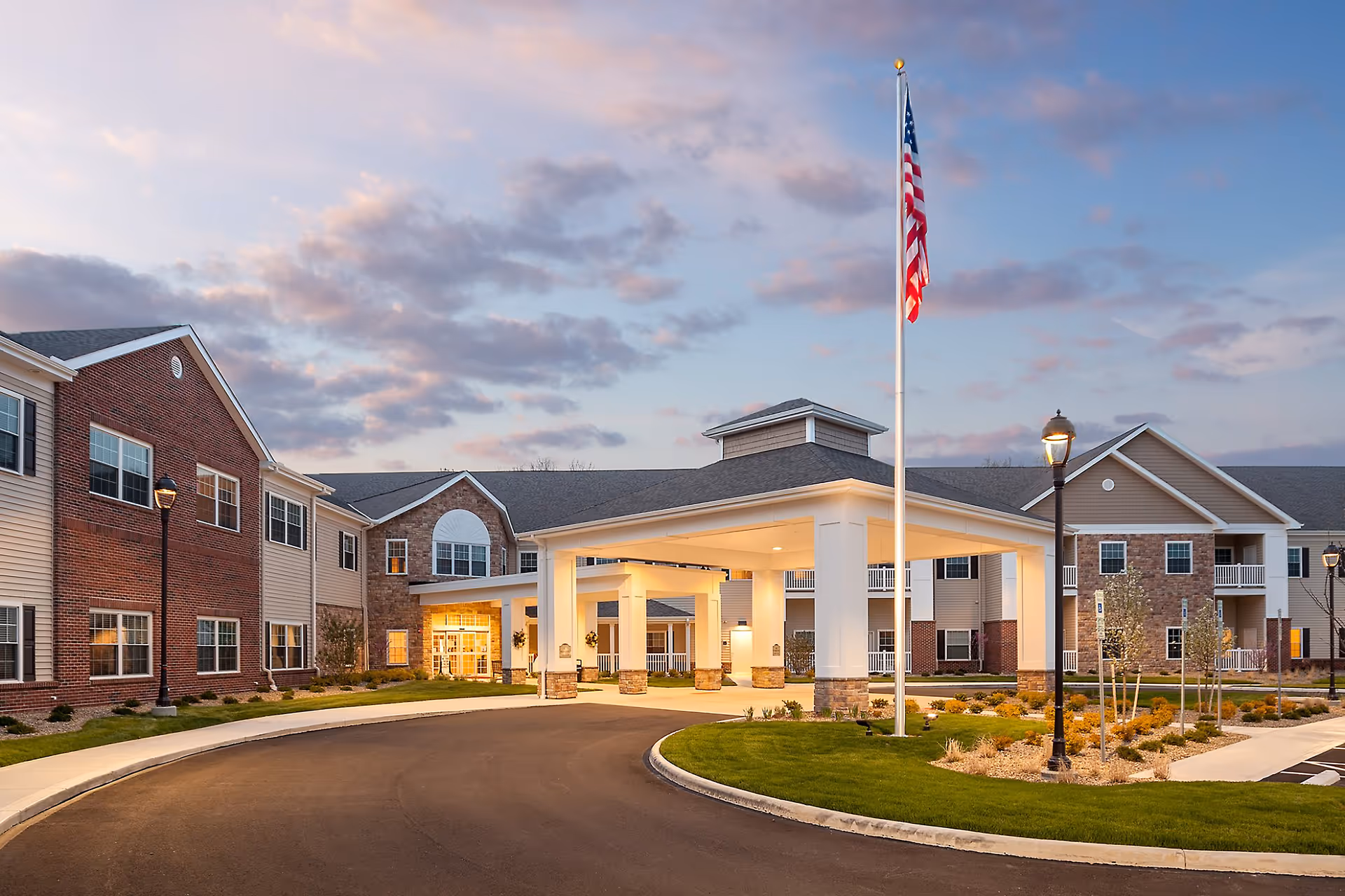 Senior living facility exterior with a covered entrance, flagpole, and circular driveway.
