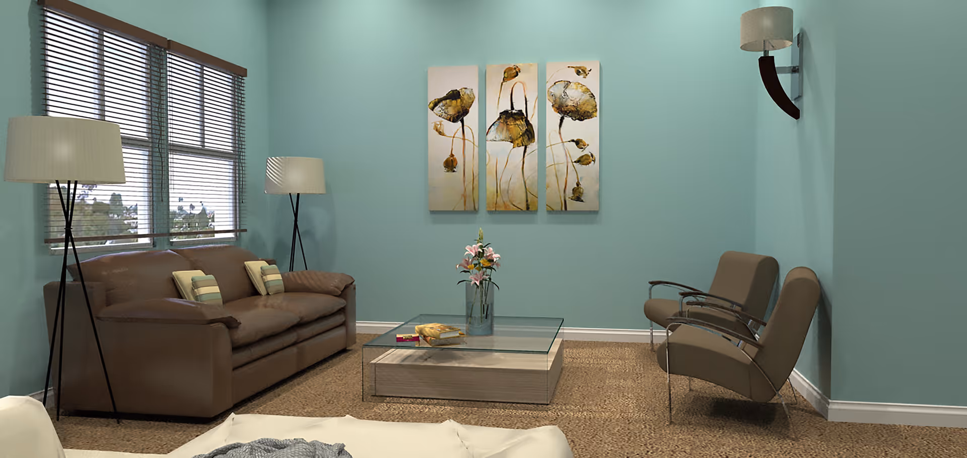 A cozy living room with teal walls, a brown leather sofa with two striped pillows, two modern armchairs, a glass coffee table with a vase of flowers and books, two floor lamps, a wall-mounted lamp, and a three-panel floral artwork on the wall.