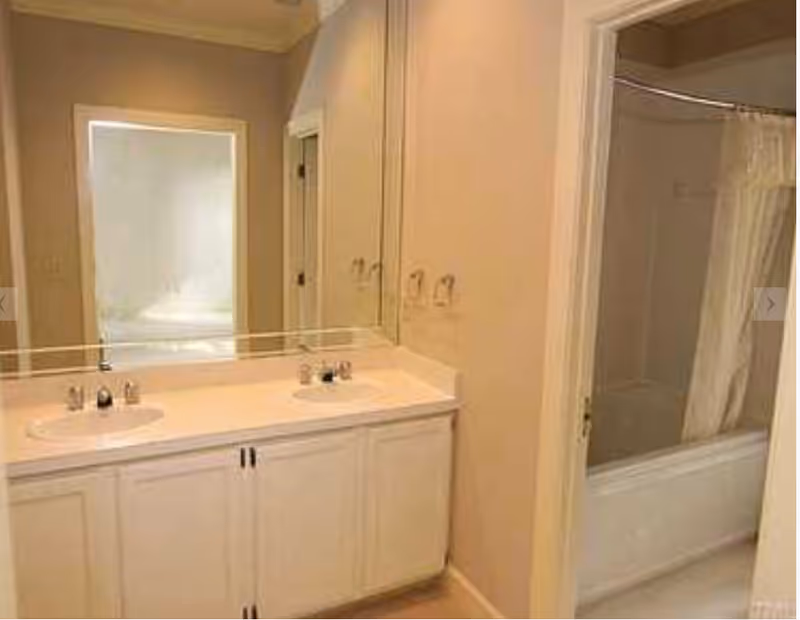 A wide bathroom vanity with double sinks, large mirror, and a bathtub with shower curtain.