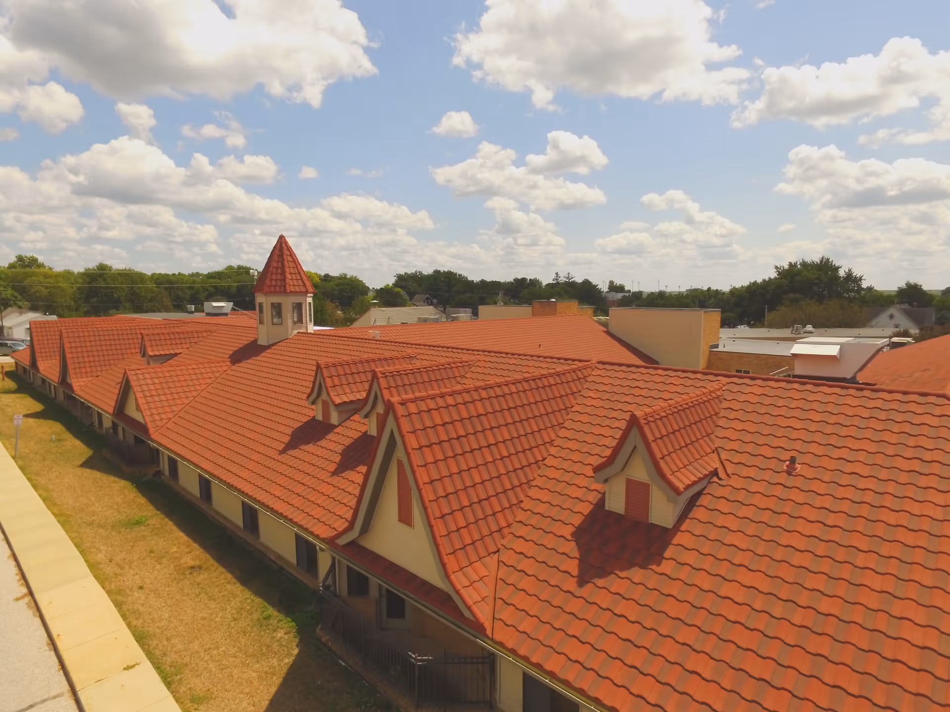 Aerial view of Salem Lutheran Homes and Rehabilitation Center showing a large building with red tiled roofs, multiple dormer windows, and a small tower with a conical roof under a partly cloudy sky.