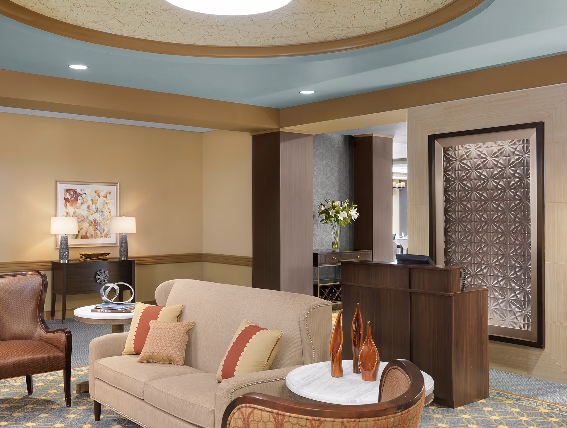 Well-appointed senior living lobby with a sofa and chairs arranged around side tables, decorative vases, artwork, and a reception desk.