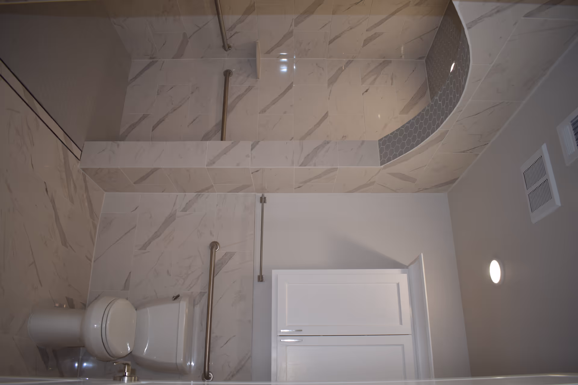Tiled bathroom with a toilet, grab bars, and a walk-in shower area.