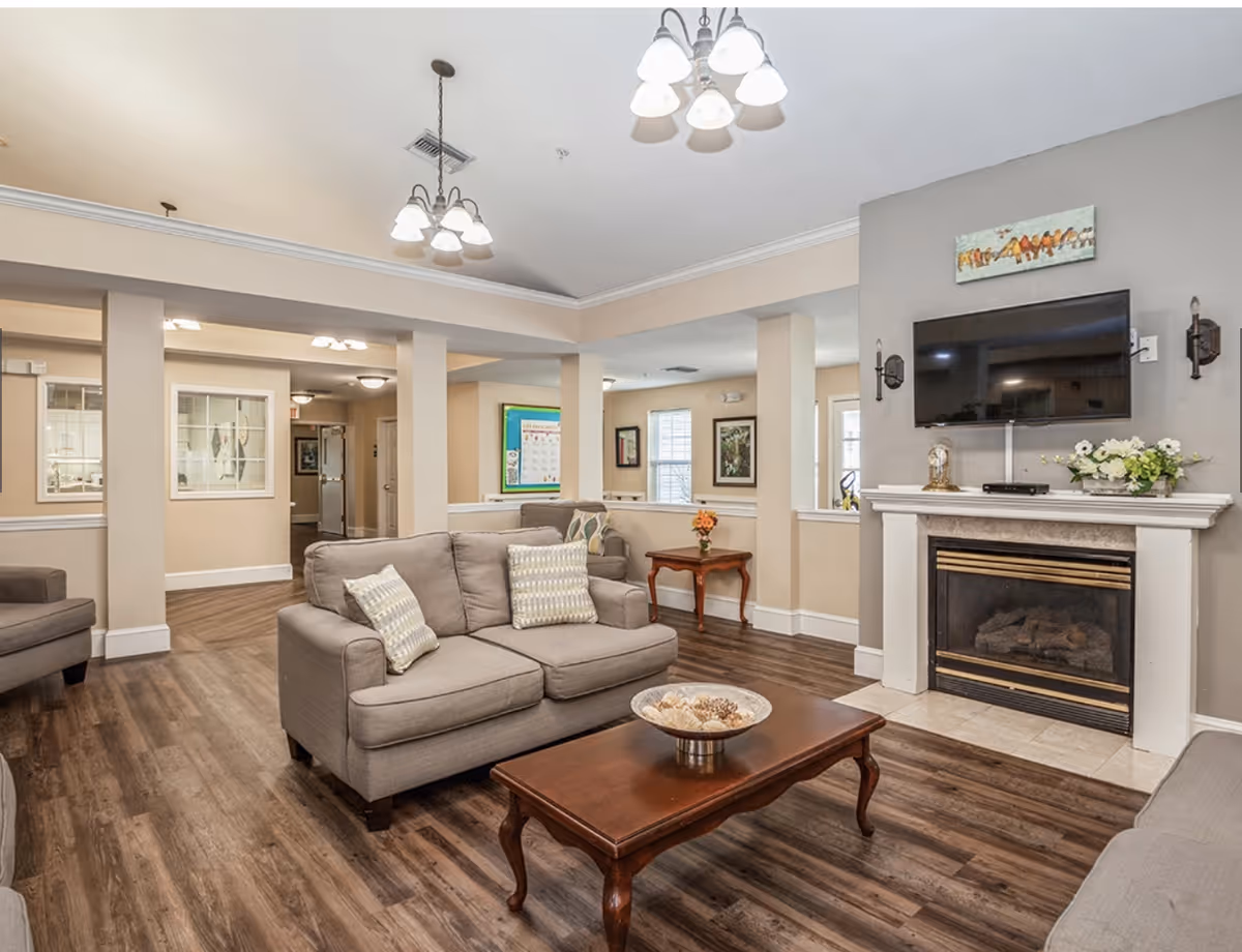 Well-lit communal living room with sofas, a coffee table, fireplace and wall-mounted TV.