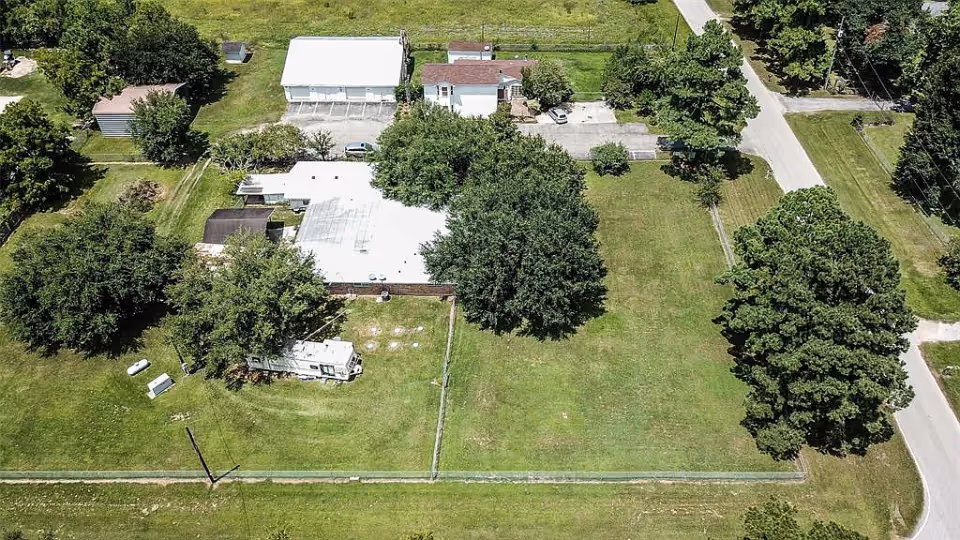 Aerial view of a property with several buildings, parking areas, and large grassy spaces with trees, surrounded by roads and open fields.