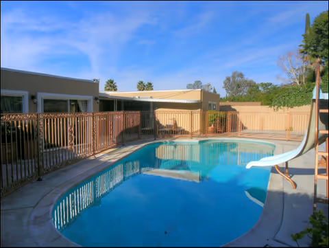 Outdoor pool area with a fenced deck, lounge chairs, and a slide at Laurelwood Villa.