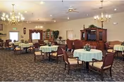 Spacious dining room with round tables covered in green tablecloths and chandeliers.