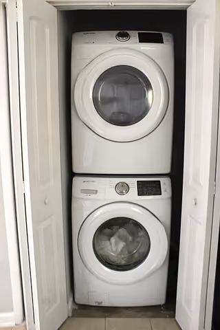 A stacked washer and dryer set inside a small closet with white bi-fold doors partially open, showing the front-loading machines in a laundry area.