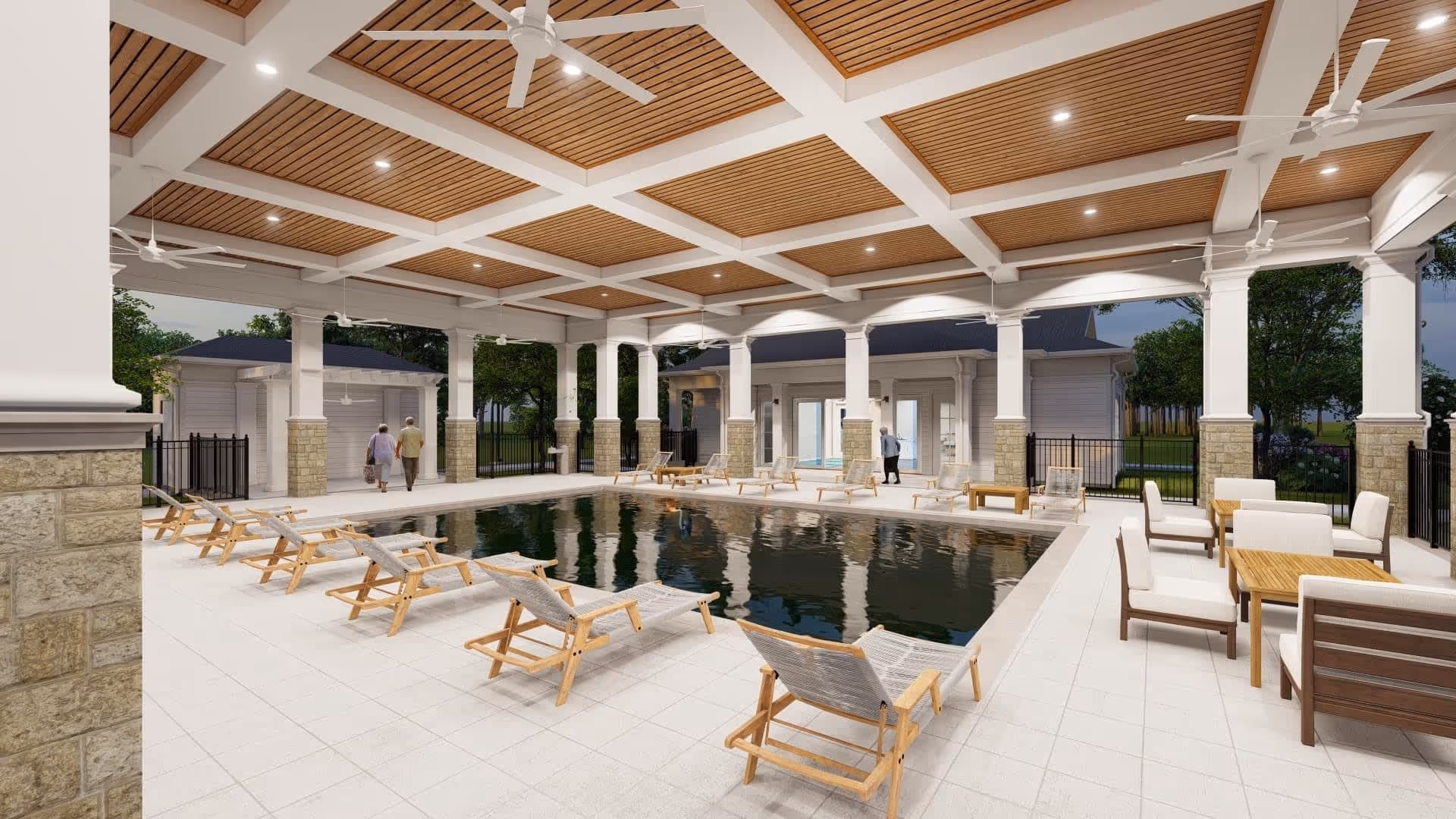 Covered outdoor pool area with wooden lounge chairs and seating tables with chairs. The ceiling has wooden panels with white beams and ceiling fans. Two elderly people walk near the pool area, and there are trees and buildings visible in the background.