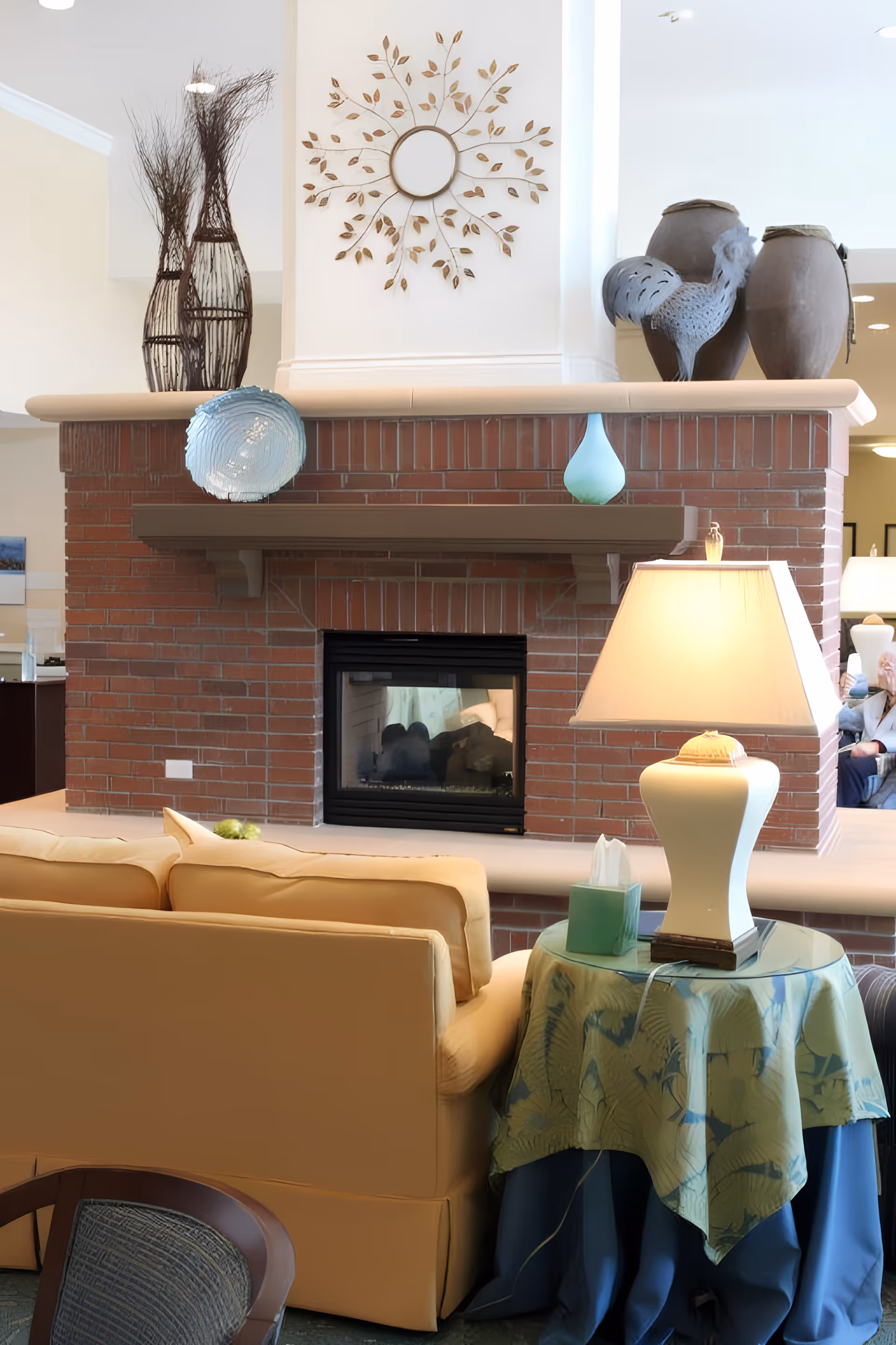 Cozy common room with a brick double-sided fireplace, sofas, decorative vases and a table lamp.