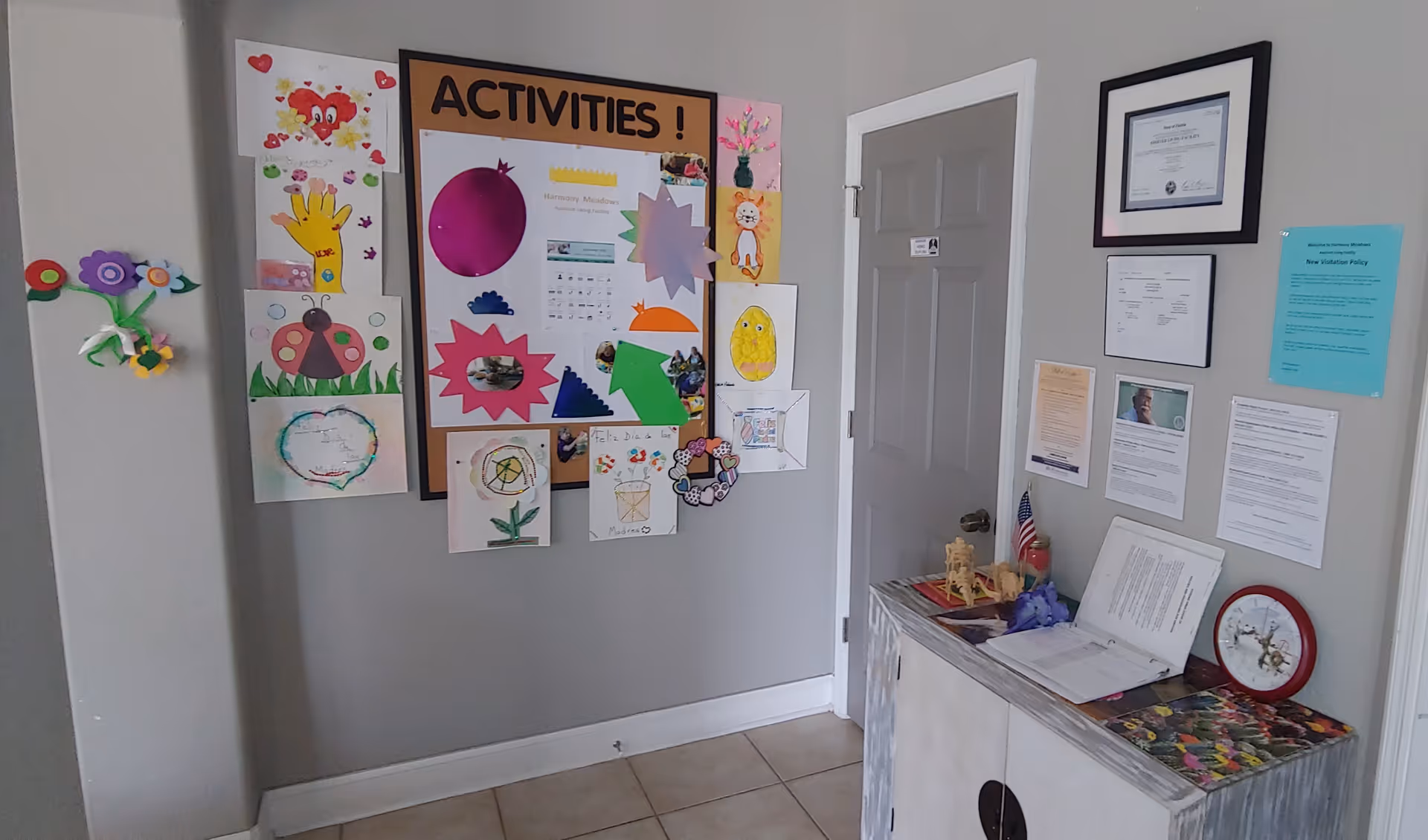 Interior hallway with an 'Activities' bulletin board displaying artwork and a small table with papers and framed notices.