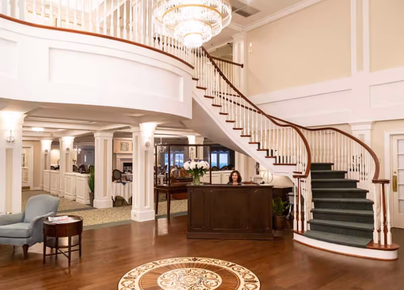 Elegant lobby with a curved staircase, reception desk, chandelier, and seating area.