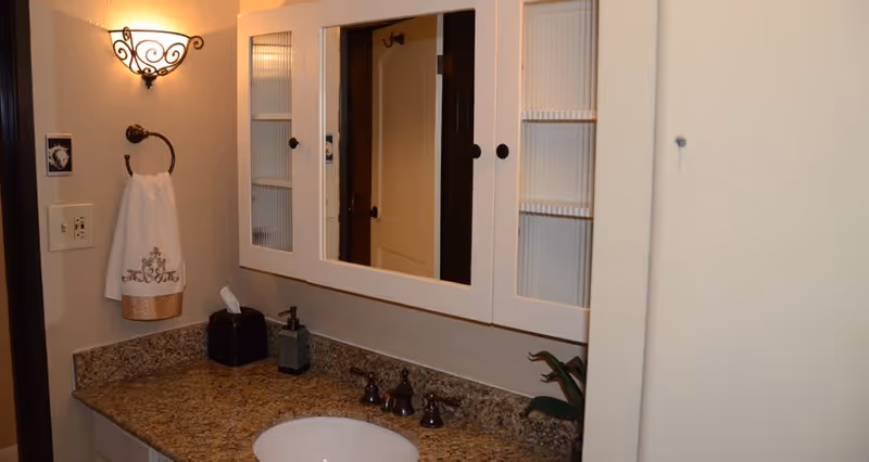 Bathroom vanity with granite countertop, undermount sink, mirrored medicine cabinet, towel ring and wall sconce.