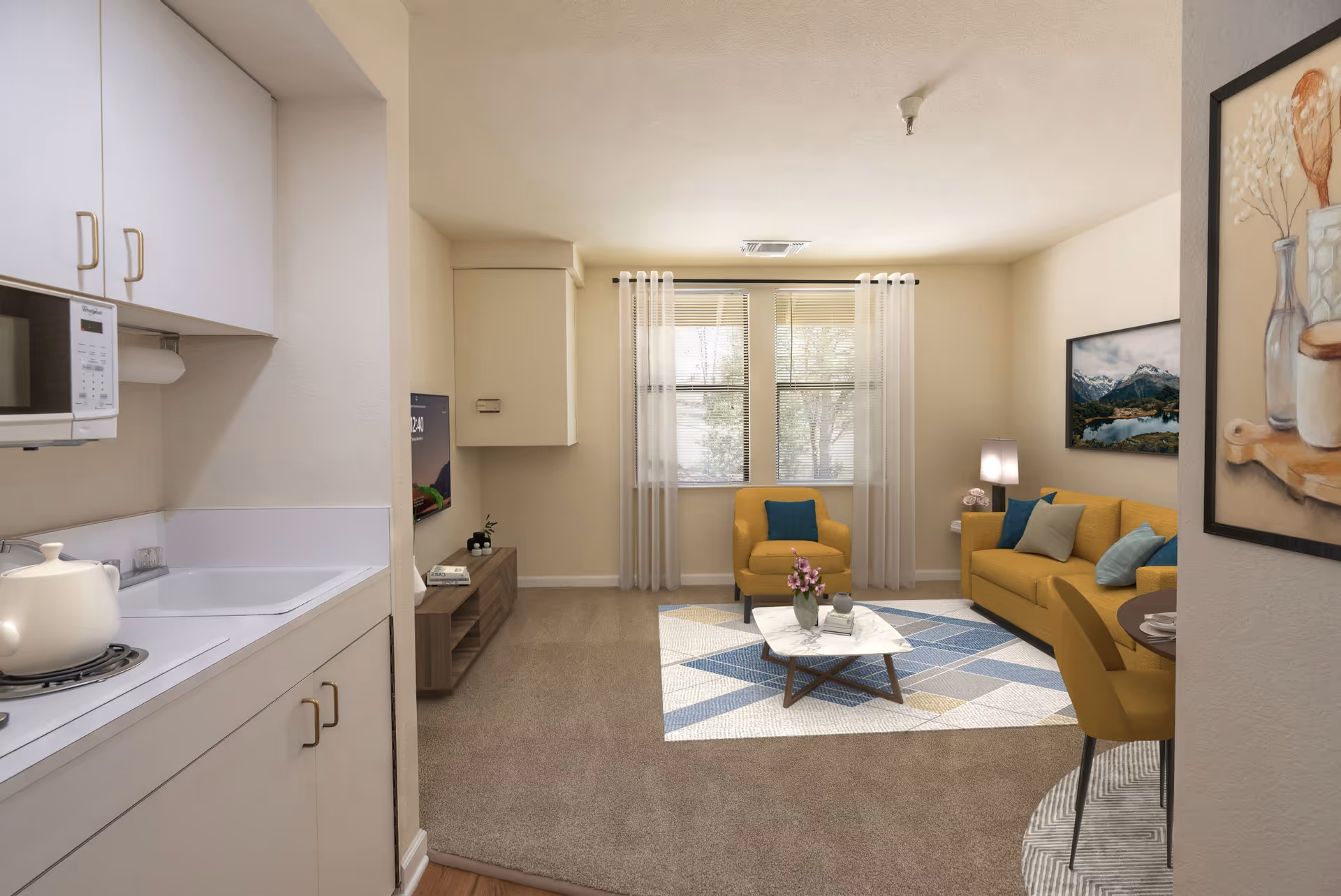 Interior view of a senior living facility apartment showing a small kitchen area with white cabinets and a microwave on the left, and a living room with mustard yellow armchair and sofa, a coffee table with flowers, a TV mounted on the wall, and a window with sheer curtains letting in natural light.
