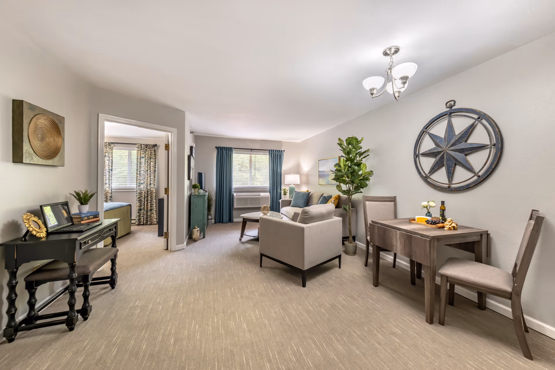 Bright open living and dining area with a sofa, coffee table, small dining table, desk, and a doorway to a bedroom.
